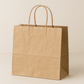 A medium-sized twisted handle bag made from durable brown Kraft paper. The bag stands upright with its top open, showing the spacious interior. It features strong twisted paper handles securely attached to the top edges, capable of supporting medium-weight contents. The natural brown paper displays a subtle texture highlighting its eco-friendly properties. The bag is photographed against a neutral background with soft, even lighting that accentuates the details of the paper texture and handle construction.