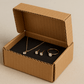 A realistic image of an open 4.7x3.5x2.5 inch corrugated cardboard jewelry box containing neatly arranged jewelry items including a delicate necklace with a pendant, a pair of earrings, and a ring. The jewelry pieces are carefully positioned inside, showcasing the box's protective qualities. The corrugated texture and fluted layers are clearly visible on the sides and edges, highlighting the box's strength despite its compact size against a simple, neutral background with soft lighting.